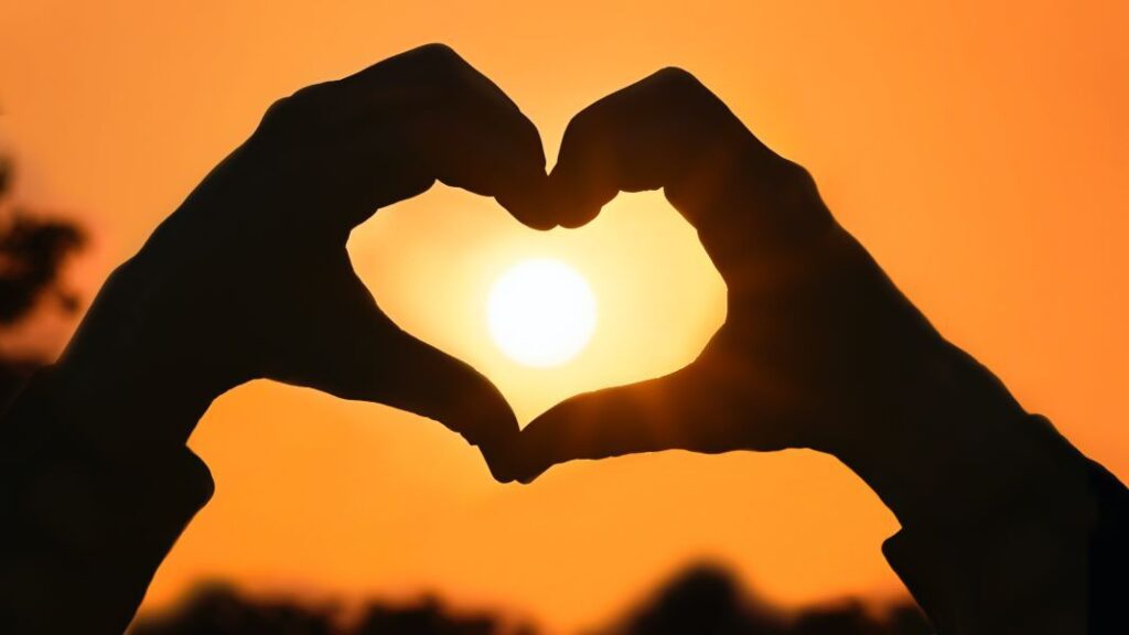 hands in the shape of a heart against an orange sky