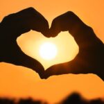 hands in the shape of a heart against an orange sky