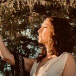 Heather Wolf with eyes closed reaching for a tree branch