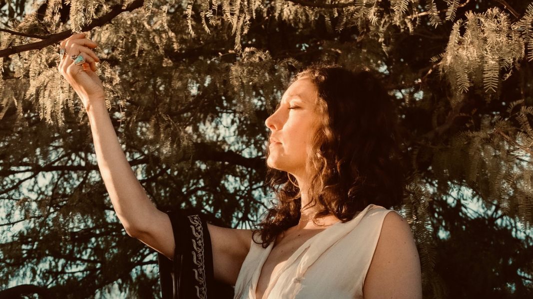 Heather Wolf with eyes closed reaching for a tree branch